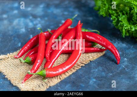 Red Hot Chili Peppers sobre un fondo oscuro en hormigón. Suplemento de comida picante. El perejil y la lechuga. Copie el espacio.