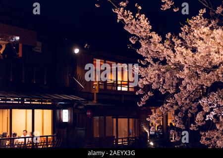 Kyoto, Japón - Abril 16, 2019: Gion en primavera durante la oscura noche negra y gente sentada comiendo en el restaurante Sakura iluminado por flores flores Foto de stock