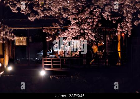 Kyoto, Japón - Abril 16, 2019: Gion en primavera durante la oscuridad de la noche y la gente sentada y comiendo en el restaurante izakaya Namisato iluminada por sakura flores Foto de stock