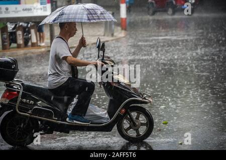 Chengdu, China - Julio 2019 : hombre chino cabalgando sobre un scooter y sosteniendo paraguas durante la lluvia tropical monzónico en Chengdu, provincia de Sichuan Foto de stock