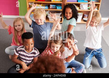 Los alumnos de primaria levantando las manos para responder a la pregunta como profesora Lee la historia en el aula
