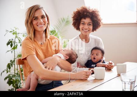 Retrato de dos madres con bebés reunión en torno a una mesa a jugar la fecha en casa