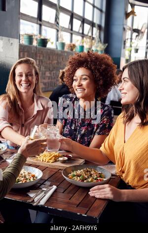 Cuatro amigas jóvenes reunión de bebidas y alimentos para hacer un brindis en el restaurante