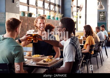Tres jóvenes amigos varones reunión de bebidas y alimentos para hacer un brindis en el restaurante