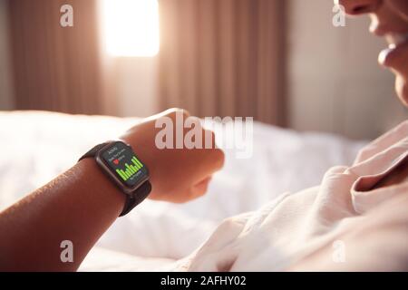 Mujer sentada en la cama mirando la pantalla de reloj inteligente