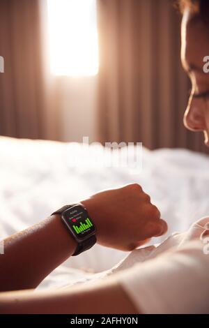 Mujer sentada en la cama mirando la pantalla de reloj inteligente