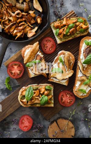 Cocinar las setas. Boletus y Cantharellus hongos en los sándwiches con tomate y albahaca sobre fondo oscuro vista desde arriba. Low Key bodegón con NAT Foto de stock