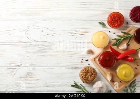 Sabrosas salsas en cuencos, especias y junta sobre fondo de madera, vista superior Foto de stock