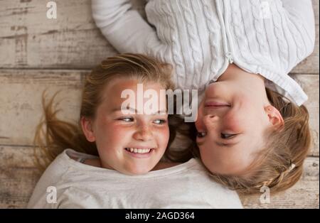 Dos hermanas sonriendo el uno al otro mientras está acostada de lado a lado sobre un piso de madera. Foto de stock