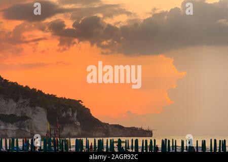 Vista de la bahía de Peschici al atardecer: Playa de arena con sombrillas, Italia (Puglia). Peschici es famoso por sus resorts junto al mar. Foto de stock
