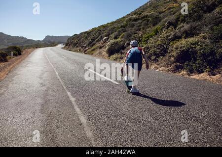 Vista posterior de la chica con el monopatín en permanente country road, Ciudad del Cabo, Western Cape, Sudáfrica Foto de stock