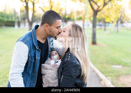 Felices padres besándose en el parque, con su hijo entre ellos
