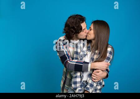 Par de camisas cuadriculada abrazar y besar aislado sobre fondo azul. Foto de stock