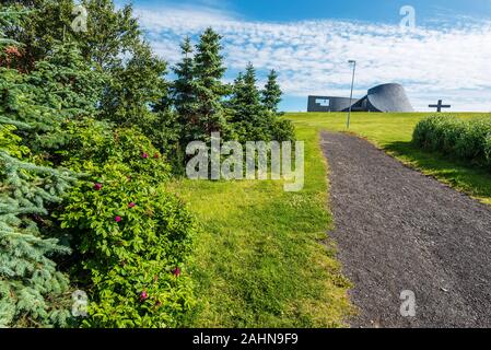 El paseo a la iglesia en Blonduos Blonduoskirkja aldea del noroeste de Islandia. Árboles y flores del parque está en primer plano.