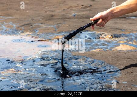 Una mano de hombre de asfalto líquido de agitación con un palo de madera en el lago Pitch, el mayor depósito natural de bitumen en el mundo. La Brea, Trinidad island, Foto de stock