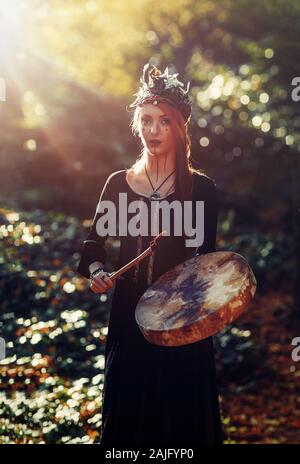 Hermosa niña jugando chamánicas chamán en tambor de bastidor en la naturaleza.