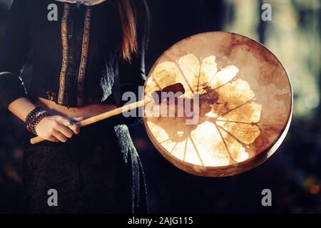 Hermosa niña jugando chamánicas chamán en tambor de bastidor en la naturaleza.