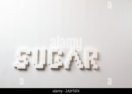 "Azúcar" escrito con pixel art letras hechas con terrones de azúcar sobre un fondo blanco. Foto de stock