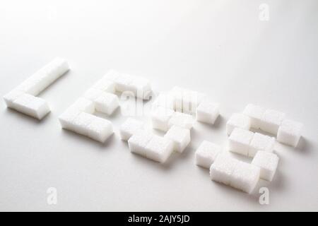 'Less' escrito con pixel art letras hechas con terrones de azúcar sobre un fondo blanco. Foto de stock