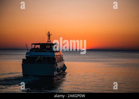 Barco turístico hacia la bella naranja puesta de sol al amanecer en el mar mediterráneo en Trieste, Italia