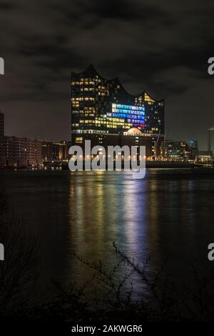 Foto nocturna de la iluminada Elbphilharmonie en el puerto de Hamburgo en la ciudad de Hafen en el río Elba con algunas reflexiones en el agua Foto de stock