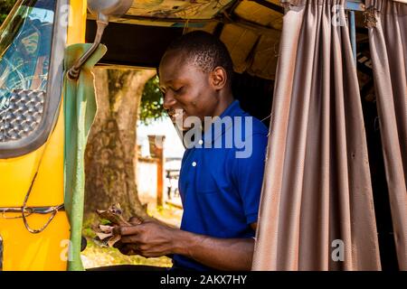 un joven africano que conduce un taxi de rickshaw contando su dinero sonriendo Foto de stock
