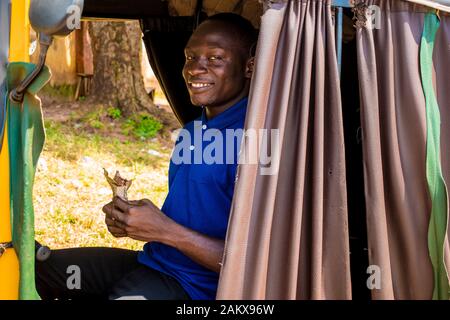 un joven africano que conduce un taxi de rickshaw contando su dinero sonriendo Foto de stock