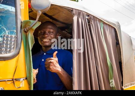 joven africano que conduce un taxi rickshaw contando su dinero sonriendo dando un pulgares para arriba Foto de stock