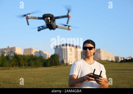 El drone compacto se desplaza delante del hombre con el mando a distancia en sus manos. El quadcopter vuela cerca del piloto. Hombre tomando fotos aéreas y videos de arriba Foto de stock
