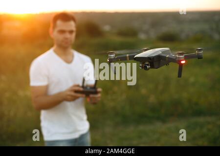 Drone se acerca delante del hombre con el mando a distancia en sus manos. El quadcopter vuela cerca del piloto. Hombre tomando fotos aéreas y videos de arriba Foto de stock