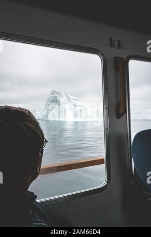 Turista Mirando los glaciares y las montañas icebergs en un barco en el oeste de groenlandia. Iceberg en el mar y el océano. Día nublado. Viajero masculino.