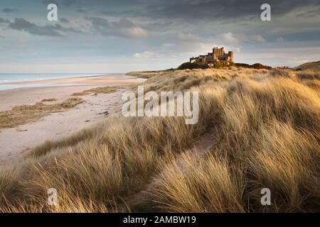 Castillo de Bamburgh al atardecer con un camino a través de las dunas de arena en primer plano.