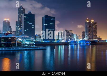 Las luces de la ciudad y el horizonte de la moderna ciudad taiwanesa Kaohsiung reflejando en el agua por la noche Foto de stock