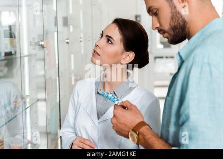 Farmacéutico y cliente con pastillas junto a vitrina en farmacia Foto de stock