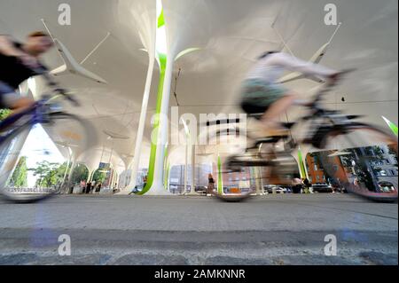 Los ciclistas pasan por la parada de tranvía y autobús de Münchner Freiheit. [traducción automática] Foto de stock