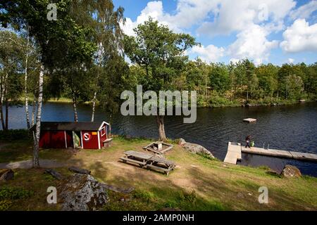 Boathouse de madera tradicional roja junto al lago en el suroeste de Suecia, Escandinavia, Europa, Madre e hijo caminando sobre un paseo de madera que sostiene las manos