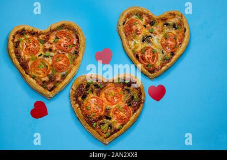 Tres pizza en la forma de un corazón sobre un fondo azul con corazones rojos. Pedir una pizza para una cena romántica en el día de San Valentín. Amor.- Foto de stock
