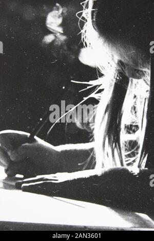 Fotografía extrema blanca y negra de los años setenta de niña escribiendo en un escritorio con retroiluminación