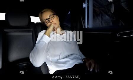 Agotado mujer dormitando en el asiento trasero del coche, ir a finales de reunión con asociados Foto de stock