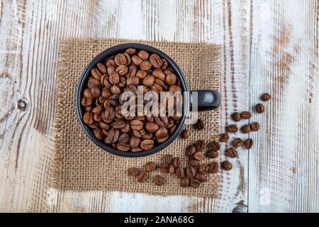 Taza de café, llena de granos de café. Los granos de café en una taza sobre fondo de madera. Foto de stock