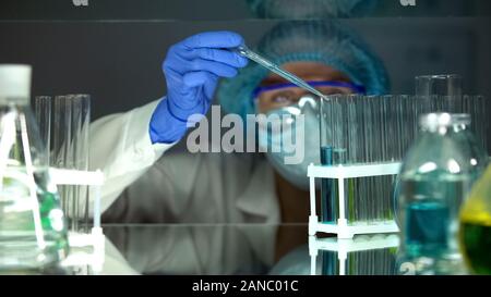 Scientist goteos de agente químico en tubo con líquido azul realizando experimento Foto de stock