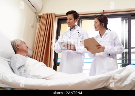 dos médicos asiáticos jóvenes que hablan con un paciente masculino asiático en la cabecera del hospital