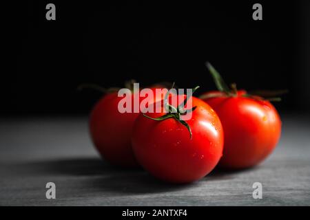 Tres tomates con gotas. Profundidad de campo completa. Tomates rojos maduros frescos para su uso como ingredientes de cocina en primer plano con copyspace en la superficie oscura Foto de stock