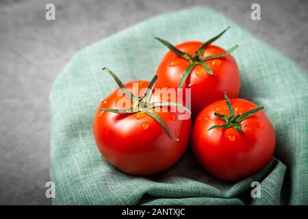 Tres tomates con gotas. Profundidad de campo completa. Tomates rojos maduros frescos para su uso como ingredientes de cocina en primer plano con copyspace en tela Foto de stock