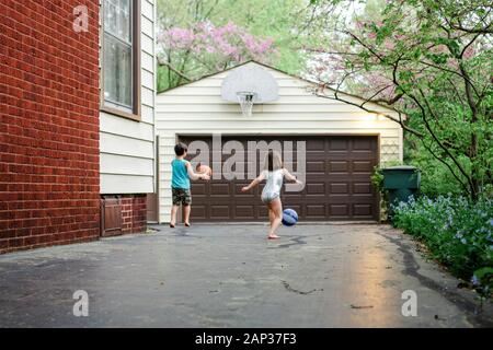 Dos niños pequeños juegan al baloncesto juntos en la entrada al atardecer