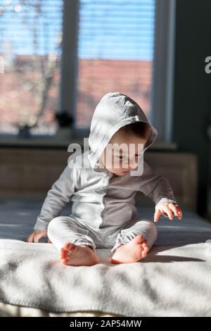 Happy Baby Boy en gris pijama sobre la cama en su habitación. Día soleado en casa dulce