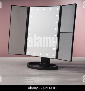 Espejo de tocador LED negro sobre mesa de madera blanca y pared rosa