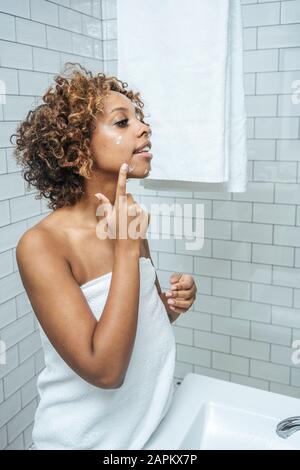 Mujer joven en el baño aplicando crema facial Foto de stock