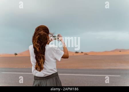 Vista posterior de la joven mujer de pie en carretera tomando fotos con smartphone, Fez, Marruecos