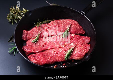 Concepto de alimentos carne cruda orgánica filete carne de ternera en sartén plancha sobre fondo negro